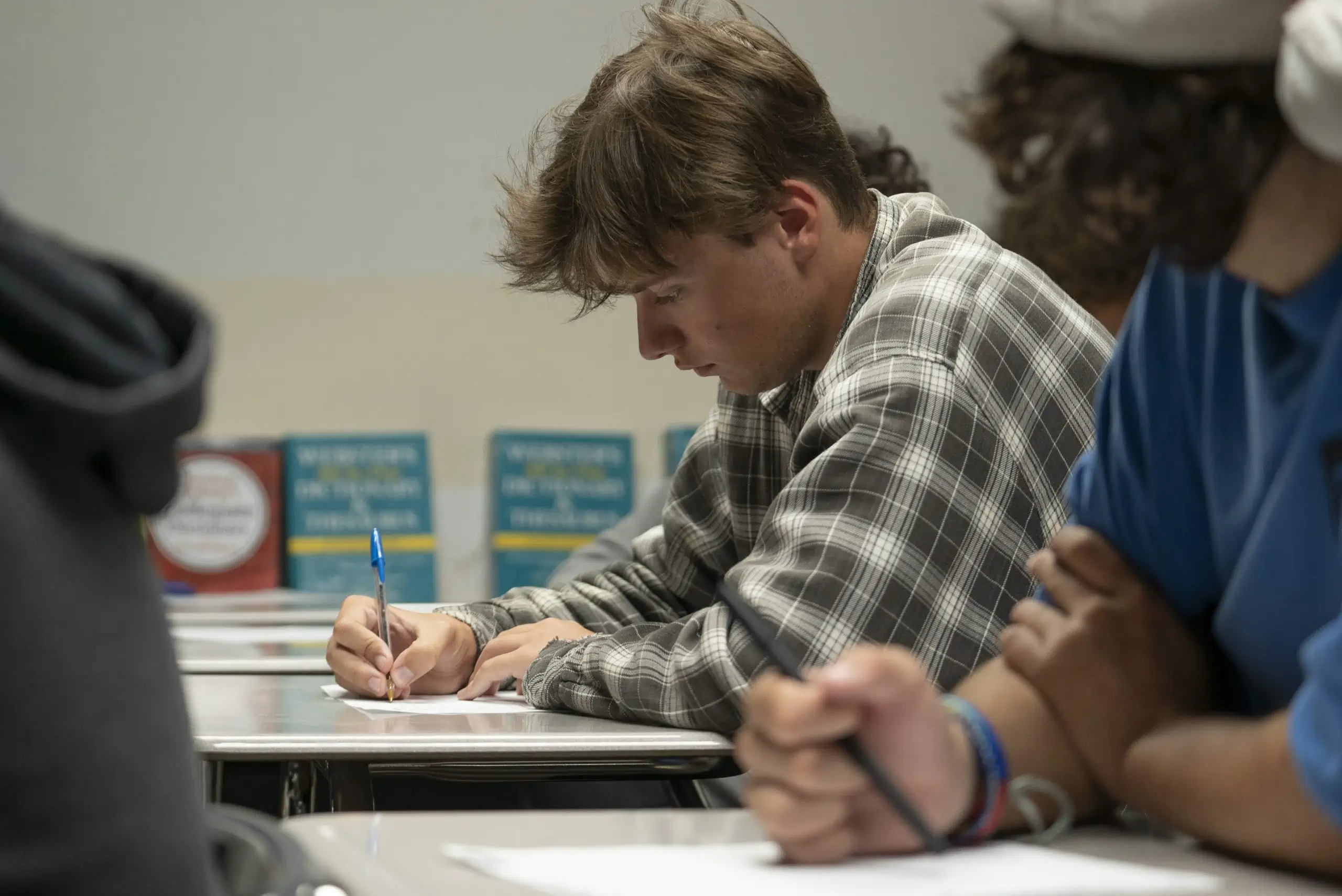 Character Education and Life Skill Training: A teenage client of Turning Winds, answering questions about his character. He is writing at a desk in a Turning Winds classroom, with two other students nearby.