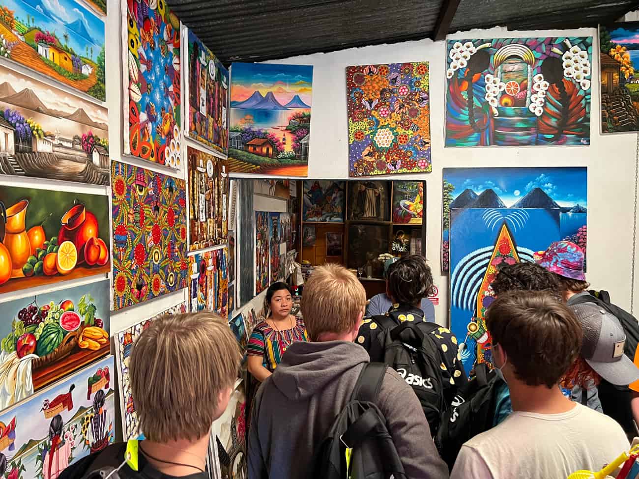 During their Guatemala service trip, students are looking at the paintings and art that are all over a vendor's walls