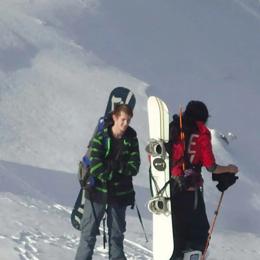 A pair of f students carrying their snowboards back up the snowy mountain for more snowboarding, one of the healthy outdoor activities Turning Winds offers.